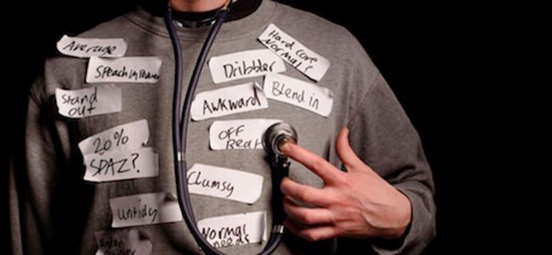 Photo of a man holding a stethoscope to his jumper which is covered in sticky labels with words written on them.
